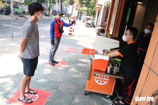 Two customers are seen standing away from each other at designated spots while waiting to pick up their drinks at a coffee shop in District 1, Ho Chi Minh City, Vietnam, March 29, 2020. Photo: Ngoc Phuong / Tuoi Tre